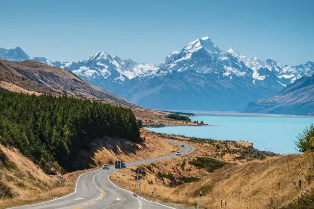 The road to Aoraki / Mount Cook beside the glacial turquoise water of Lake Pukaki, with the snow-covered Southern Alps filling the horizon.