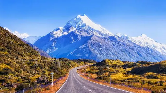 The road to Aoraki / Mount Cook, its snow-covered summit rising above tussock hillsides under a clear sky.